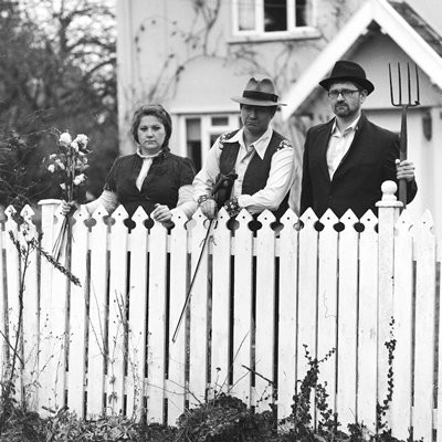 Three people standing behind a white picket fence.