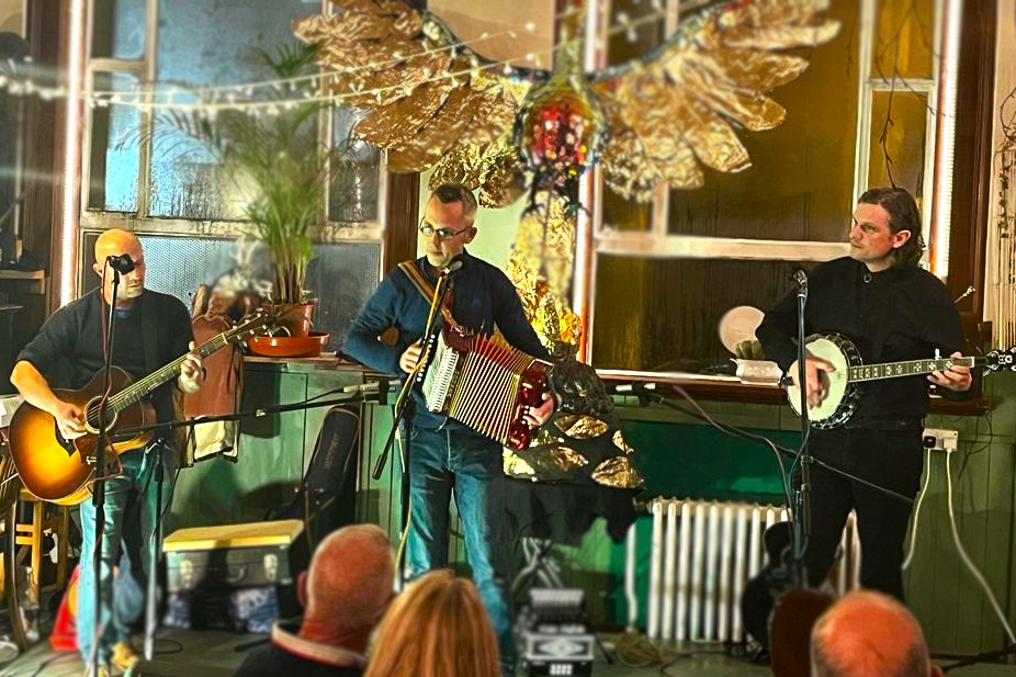 Three men, one playing guitar, one playing melodeon and one playing the banjo.
