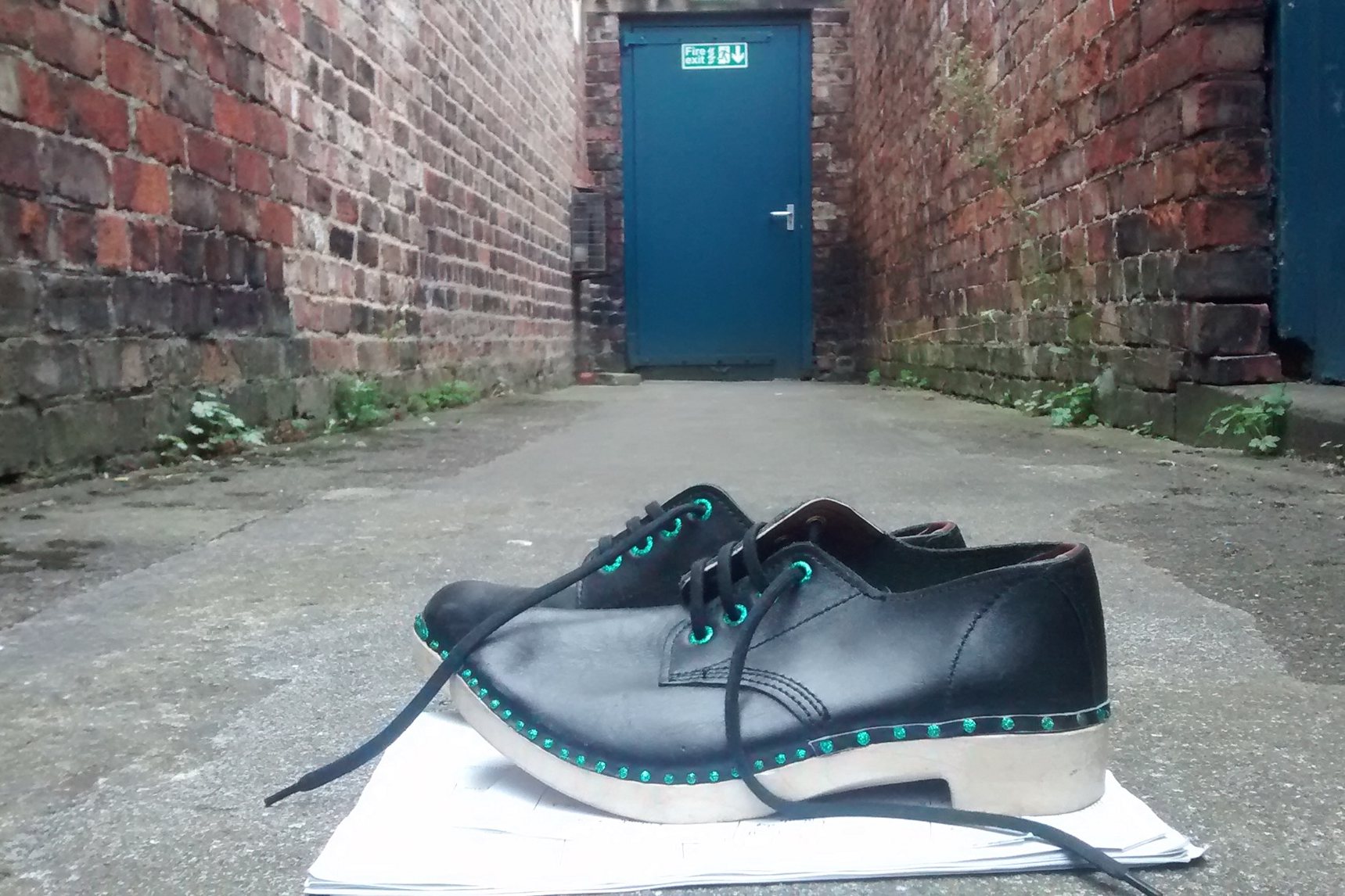 A pair of dancing shoes in front of a brick wall with a blue door.