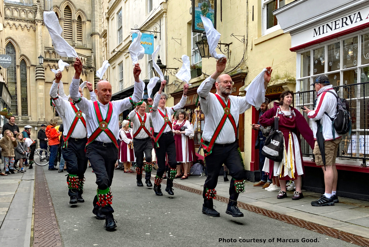 A group of morris dancers marching through a historic town centre.