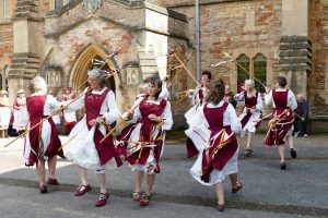 A group of dancers in maroon and white costumes dancing outside a large church building.