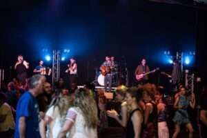 A group of people playing music on stage with people dancing in the foreground.