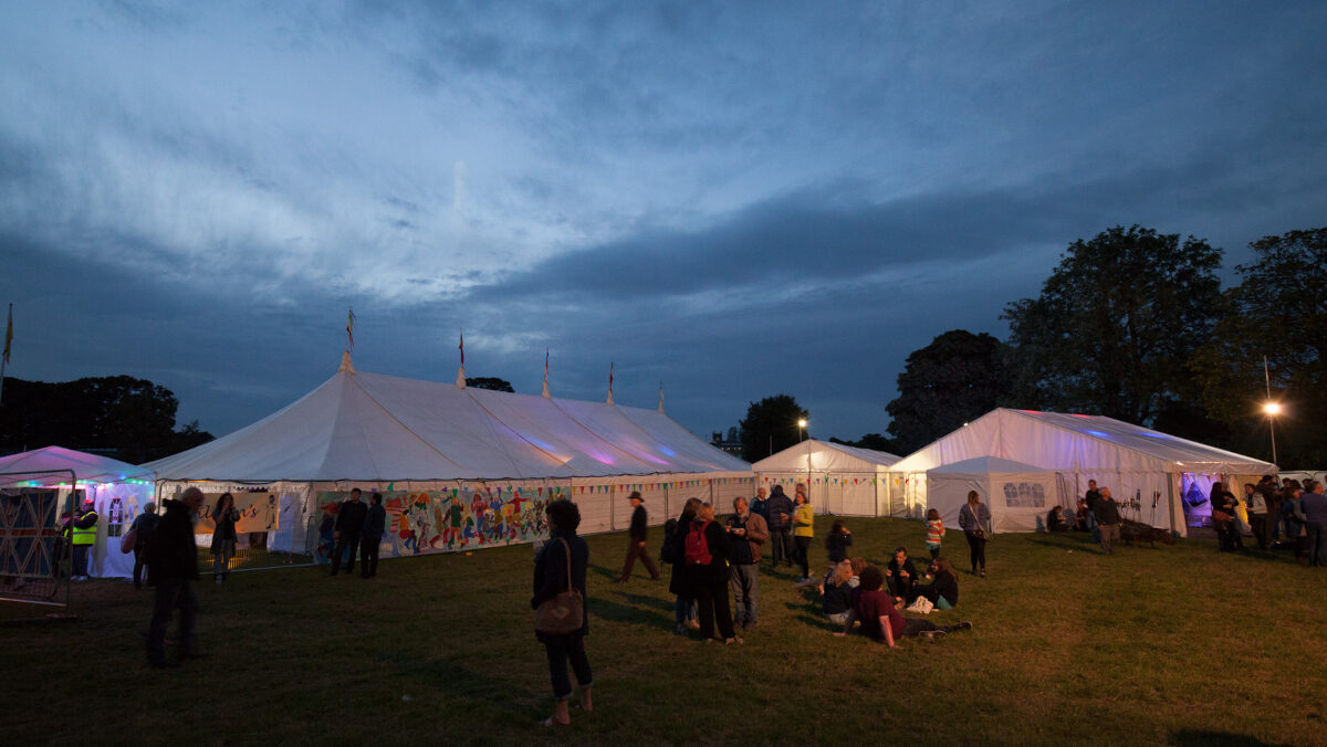 Large white marquees in a field at dusk.