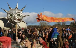Peoople in a procession with banners and masks on sticks