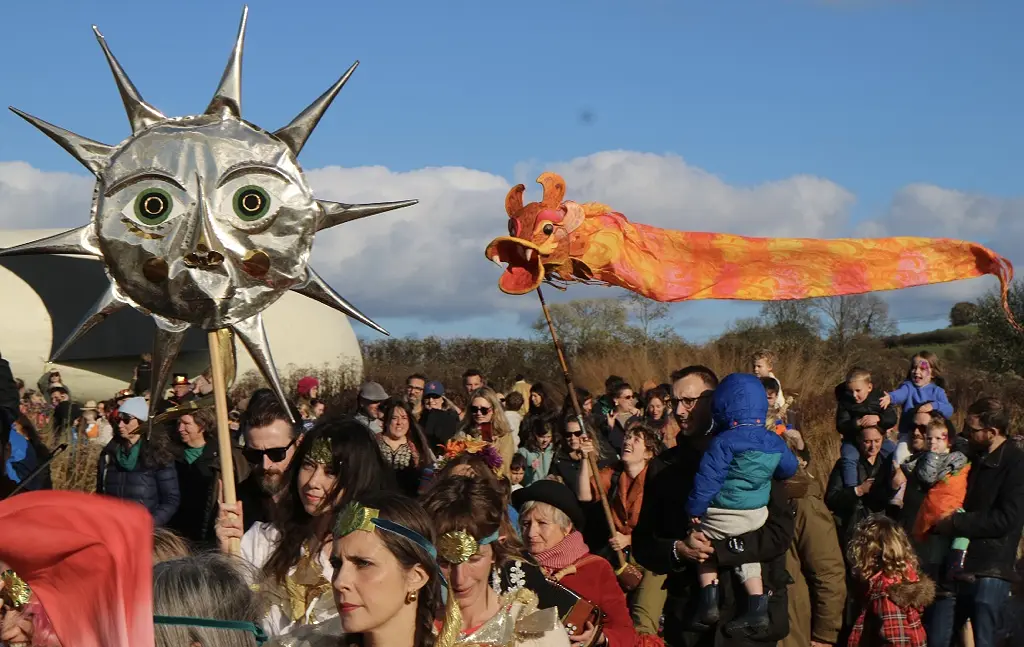 Peoople in a procession with banners and masks on sticks